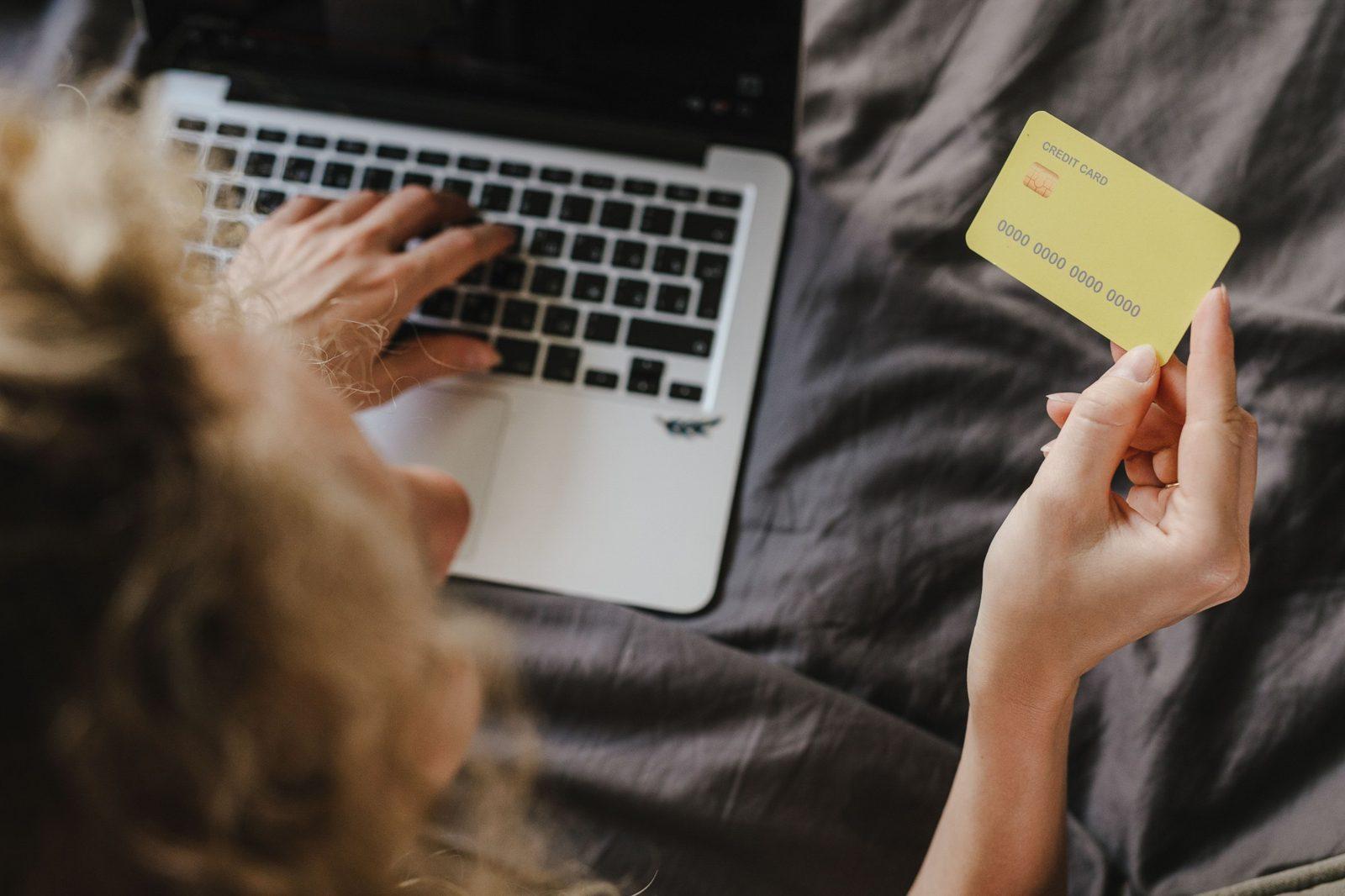 Una mujer paga por internet desde su laptop, con su tarjeta en la mano