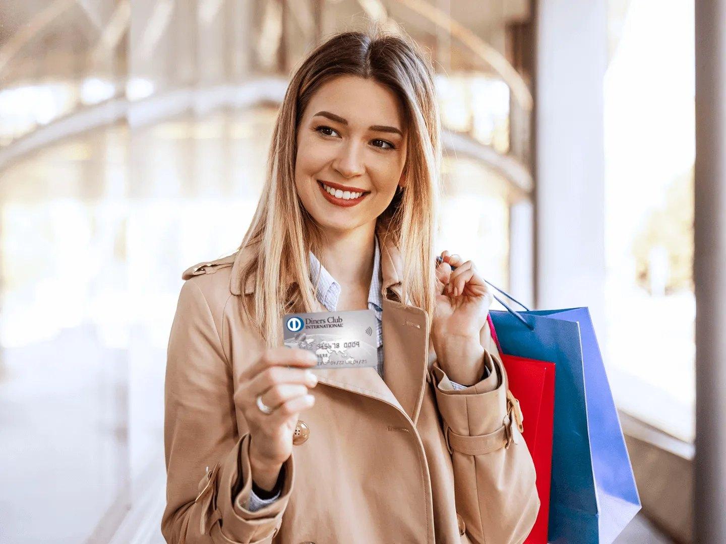 Una mujer sonriente, con bolsas de compras, muestra su tarjeta Diners Club