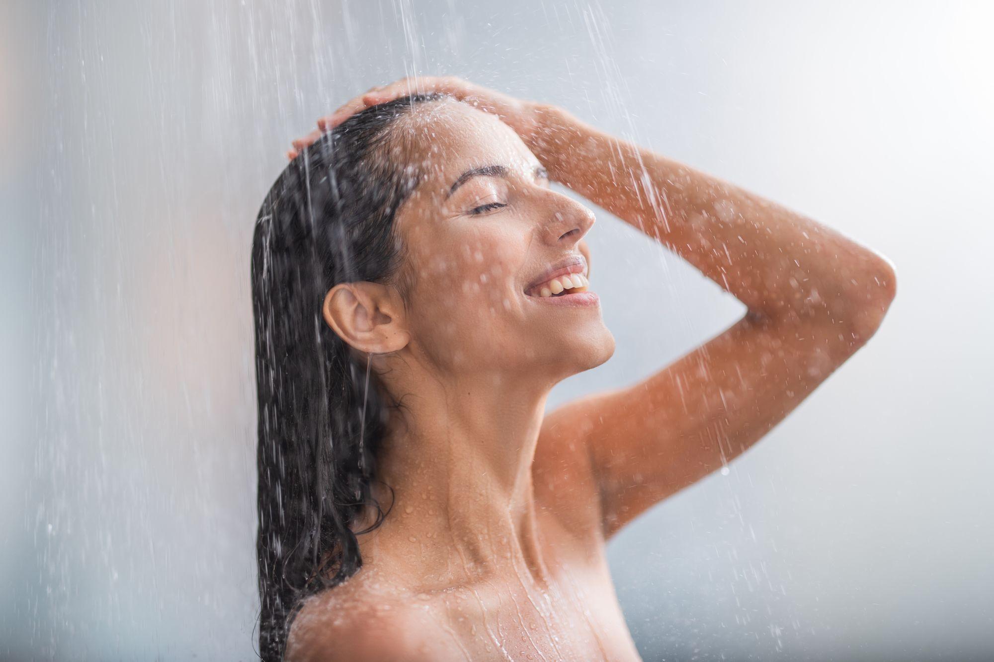 Mujer sonriente bajo el agua caliente de la ducha
