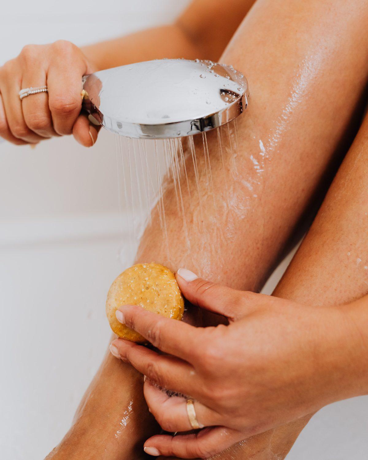 Una mano sostiene la ducha de mano mientras el agua cae sobre el brazo